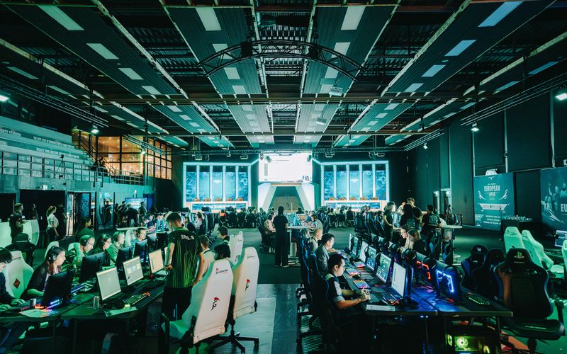 A wide view of the competition floor at the Excel Esports European Open, rows of stations under stage lighting.